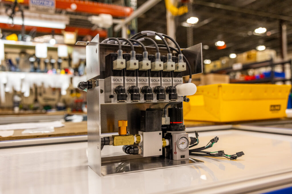Close-up of a six-valve manifold with labeled solenoids SOL1–SOL6 and attached tubing in a factory setting.
